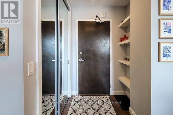 Interior apartment hallway with dark wood door, mirrored closet, and shelving unit. - 912 - 112 King Street E, Hamilton