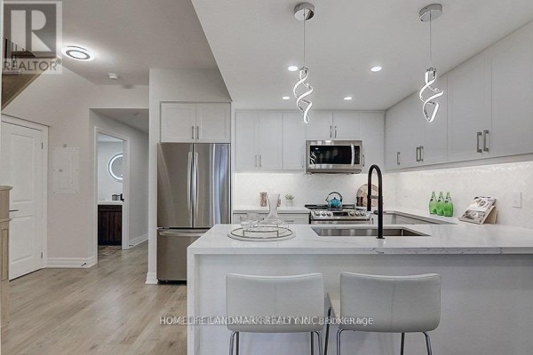 View of a white kitchen with stainless steel refrigerator and island, leading to a hallway. - 912 - 8110 Birchmount Road, Markham