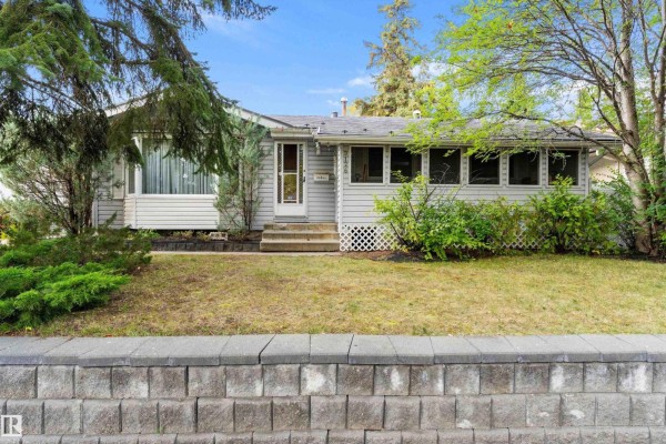 A white-gabled bungalow with gray siding and a covered porch, set back from a paved sidewalk and street. - 9126 92 Av, Fort Saskatchewan