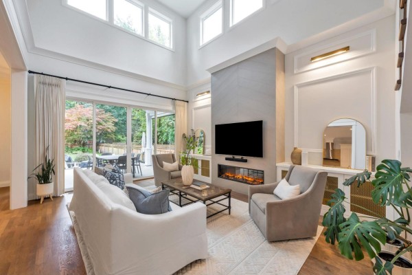 Living room with vaulted ceiling, fireplace, white sofa, and glass doors to patio. - 9128 Edal Street, Langley