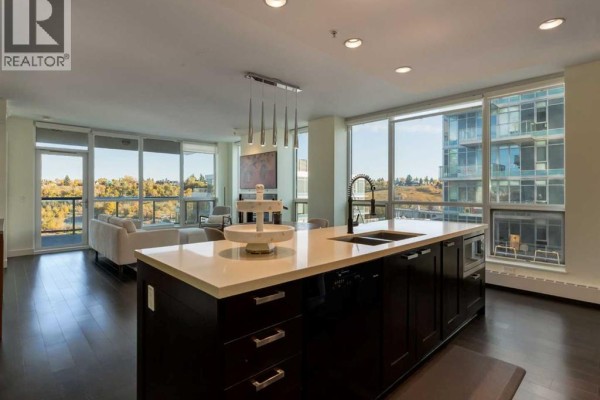Open concept living room and kitchen with a large island, dark cabinets, and city views. - 913, 222 Riverfront Avenue Sw, Calgary