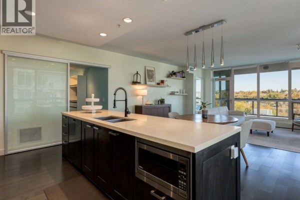 Modern kitchen island with a sink, pendant lights, and view of the dining area and living room. - 913, 222 Riverfront Avenue Sw, Calgary