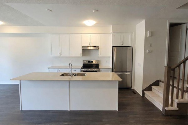 Kitchen and dining area with white cabinets, stainless steel appliances, island, and stairs. - 913 - 585 Colborne Street E, Brantford