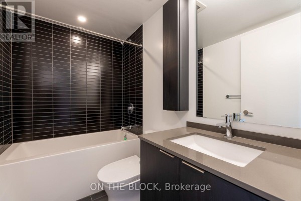 Modern bathroom with black tiled shower walls, white tub, and vanity. - 913 - 86 Dundas Street E, Mississauga
