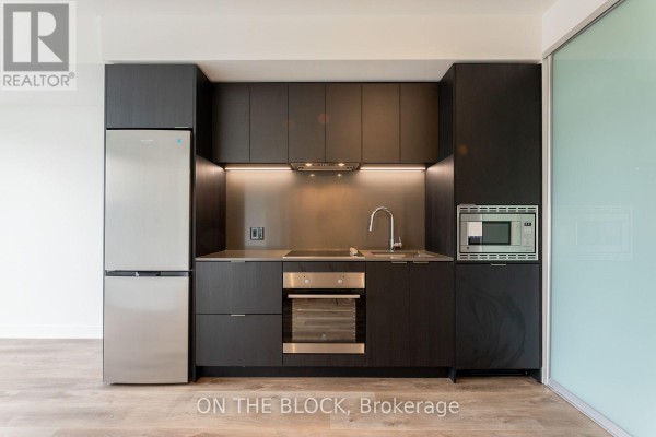 Compact kitchen featuring dark wood cabinets, stainless steel appliances, and a microwave. - 913 - 86 Dundas Street E, Mississauga