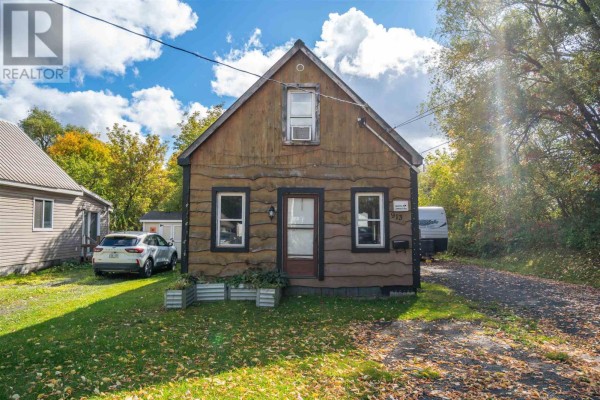 Close-up of the rustic wooden house exterior featuring multiple windows and a brown front door. - 913 Bonney St, Sault Ste  Marie