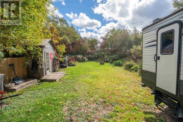View of the backyard showing a large grassy area with a small shed and a travel trailer. - 913 Bonney St, Sault Ste  Marie