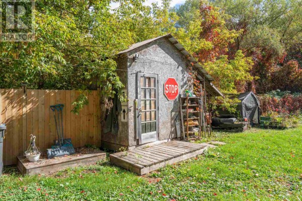 A small wooden shed with a glass door and a stop sign mounted on the front, set in a grassy backyard. - 913 Bonney St, Sault Ste  Marie