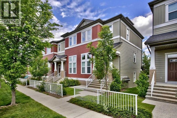 Side view of the townhouse exterior showcasing red siding and adjacent units with white railings. - 913 Evanston Square Nw, Calgary