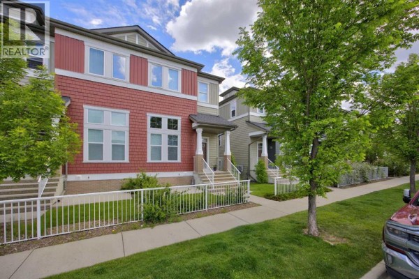 Street view of a townhouse complex with multiple units featuring red and green siding and mature trees. - 913 Evanston Square Nw, Calgary