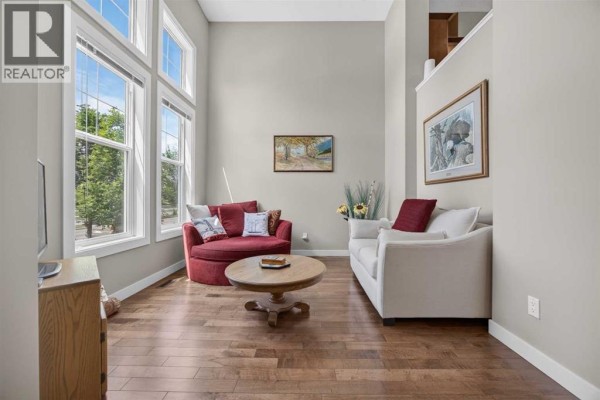 Living room with a red sofa, white armchair, wooden coffee table, hardwood floors, and stairs. - 913 Evanston Square Nw, Calgary