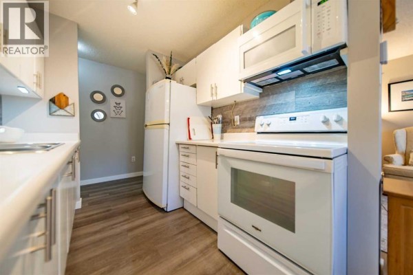 Kitchen with white cabinets, a white stove and oven, a microwave, and a refrigerator. - 914, 11620 Elbow Drive Sw, Calgary