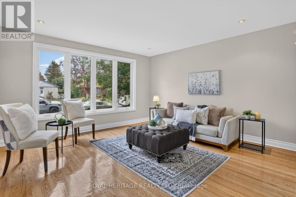 Living room with a large bay window, hardwood floors, a couch, and an ottoman. - 914 Donovan Crescent, Whitby