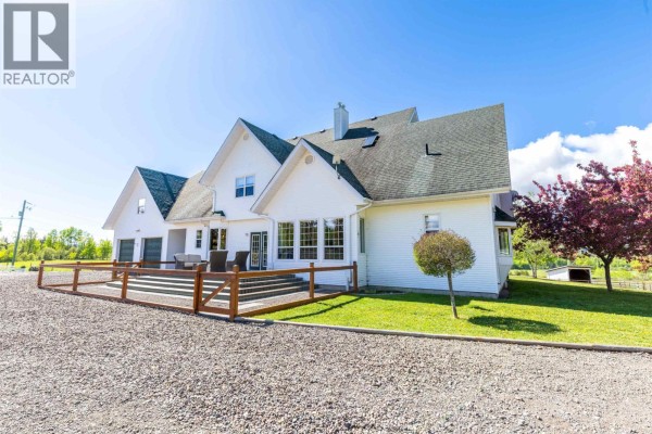 White house with a driveway, wooden fences, green fields, and snow-capped mountains. - 9146 Engman Road, Smithers