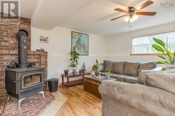 Basement living room with a brick hearth wood stove, gray sectional sofa, and wood floors. - 9147 201 Highway, Nictaux
