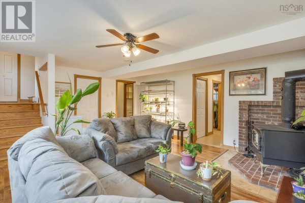 Living room with a wood stove, sofa, stairs, and doorways to other rooms. - 9147 201 Highway, Nictaux