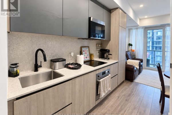 Modern kitchen with stone backsplash, black faucet, stainless steel microwave, and wood cabinets. - 915 - 108 Peter Street, Toronto
