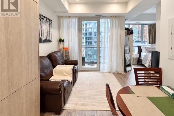 Living area with brown leather sofa, white rug, and floor-to-ceiling curtains covering a city view. - 915 - 108 Peter Street, Toronto