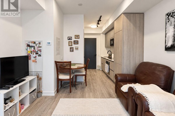 Living room with a TV on a white shelf unit, small dining table, and leather sofa in front of a balcony. - 915 - 108 Peter Street, Toronto