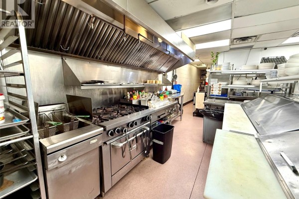 Commercial kitchen with stainless steel range, deep fryers, and shelving units. - 915 Fort St, Victoria