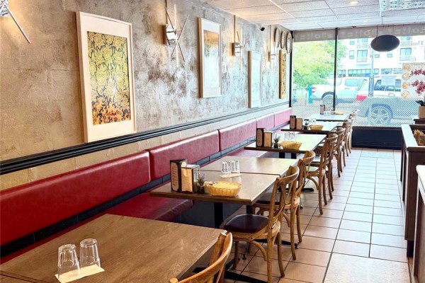 Restaurant seating area with red banquette, wooden chairs, and framed artwork on a textured wall. - 915 Fort St, Victoria