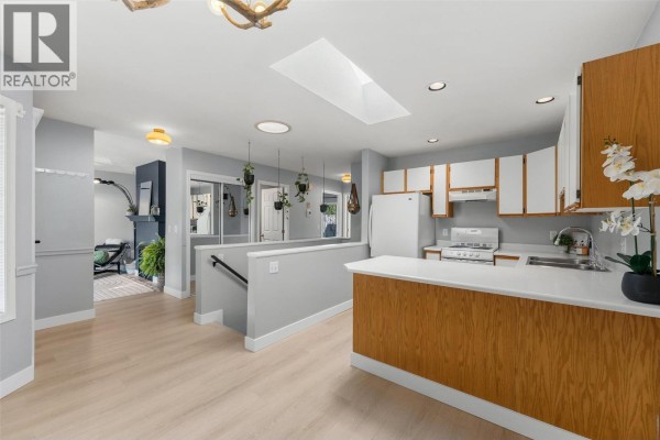 Kitchen with white counters, wood cabinets, and hanging plants above a gray island. - 9159 Glenmore Road Unit# 1, Lake Country