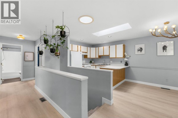 Kitchen area with white cabinets, wood accents, and hanging plants near a hallway. - 9159 Glenmore Road Unit# 1, Lake Country