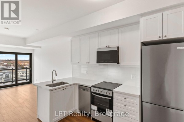 View of an L-shaped kitchen with white cabinets, stainless steel appliances, and access to a living area. - 917 - 51 Clarington Boulevard, Clarington