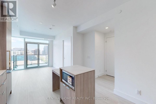 View of the kitchen island with microwave and entryway, leading to a bright living space with a balcony. - 917 - 6 Greenbriar Road, Toronto