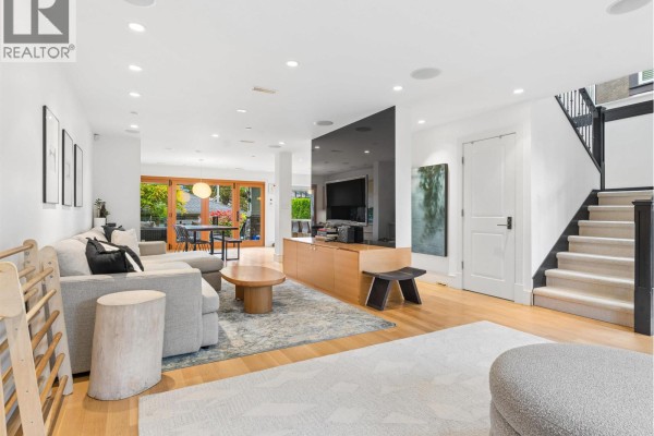 Living room with large sofa, television, dining area, and view of backyard. - 917 W 20th Avenue, Vancouver