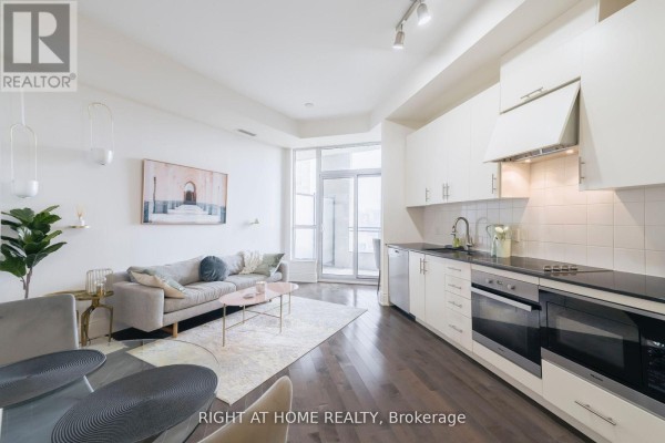 Open concept living space with sofa, coffee table, and white kitchen cabinets. - 918 - 23 Glebe Road W, Toronto