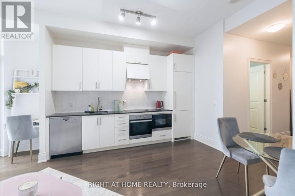 White galley kitchen with stainless steel appliances and a gray desk chair. - 918 - 23 Glebe Road W, Toronto