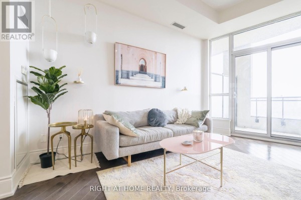 Living area with a gray sofa, pink coffee table, and a large window. - 918 - 23 Glebe Road W, Toronto