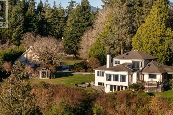 Rear view of white house with large windows and decks overlooking wooded area. - 9193 West Coast Rd, Sooke