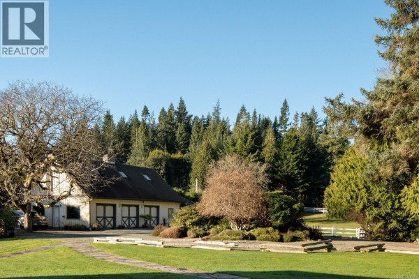 Exterior of a white barn with double doors and skylights, surrounded by trees. - 9193 West Coast Rd, Sooke
