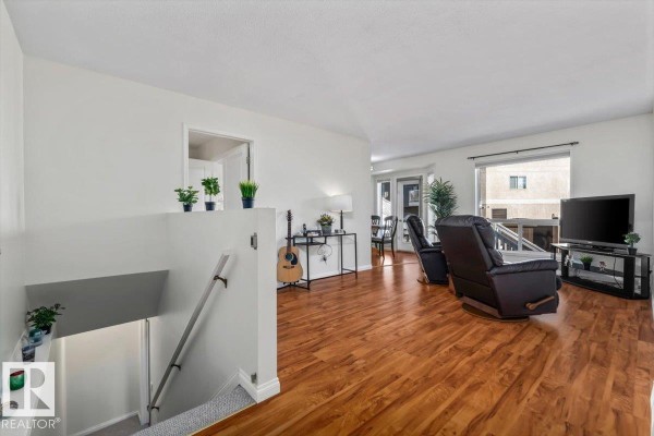 Living room with wood floors, white walls, a television, fireplace, and large window. - #92 13320 124 St Nw, Edmonton