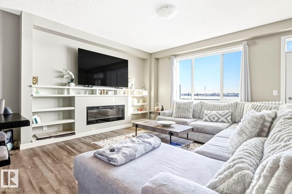 Living room with large sectional couch, fireplace, entertainment unit, and large window. - #92 16903 68 St Nw Nw, Edmonton