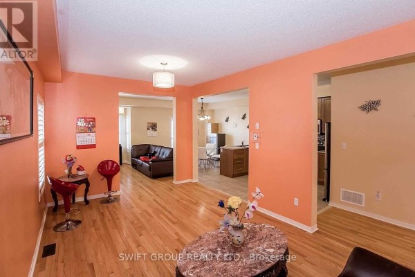 Living room with light wood floors, coral accent wall, and openings to other rooms. - 92 Checkerberry Crescent, Brampton