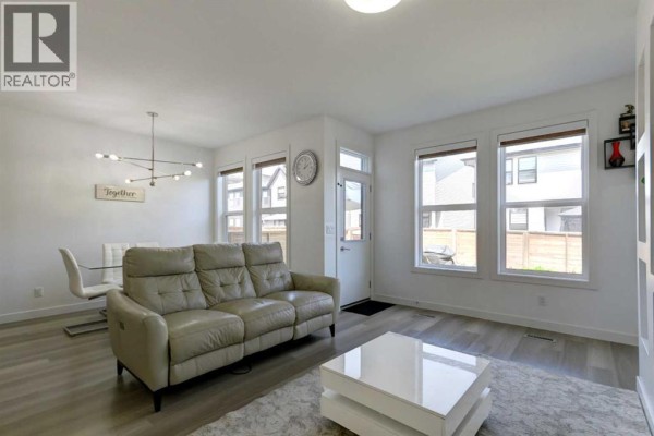 Living and dining area with a leather sofa, dining table, and large windows. - 92 Copperhead Grove Se, Calgary
