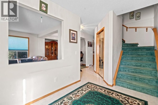 View from entryway through a pass-through to living area, with stairs and hallway visible. - 92 Del Ray Close Ne, Calgary