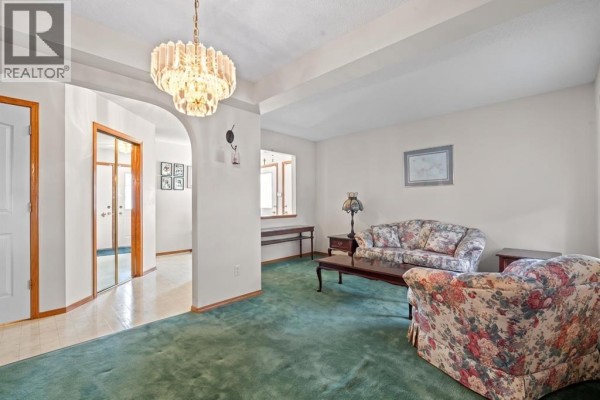 Living room with floral sofa and armchair, green carpet, and an arched entryway. - 92 Del Ray Close Ne, Calgary