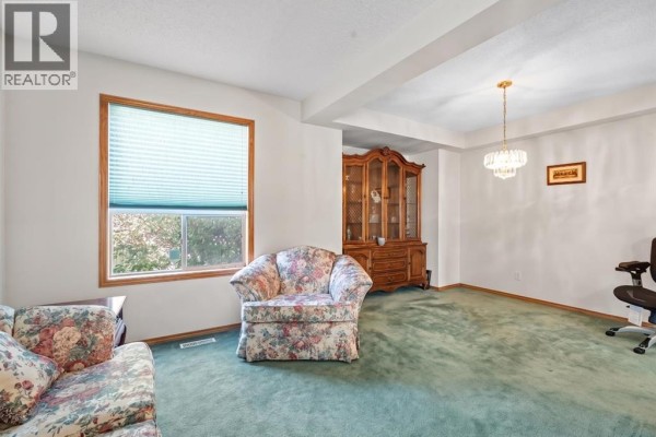 Living room with a floral armchair, window with blinds, and a wooden china cabinet. - 92 Del Ray Close Ne, Calgary