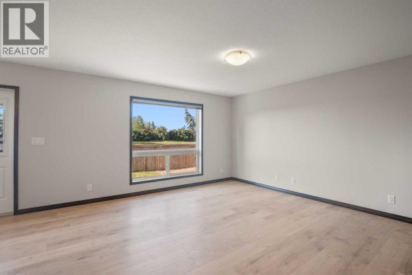 Living room with light wood floors, beige walls, and a large window overlooking greenery. - 92 Ireland Crescent, Red Deer