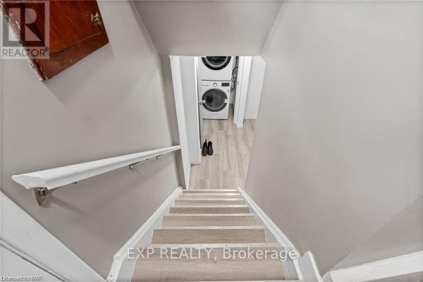 Interior view looking down wooden stairs towards a stacked washer and dryer. - Lower - 92 Margery Avenue, St  Catharines