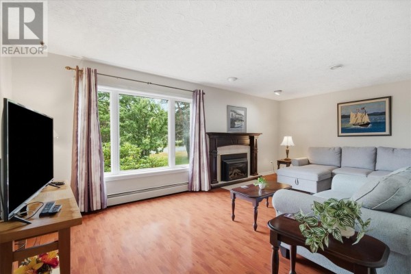 Living room with light beige walls, hardwood floors, large window with green outdoor view, and fireplace. - 92 Quigleys Lane, Torbay