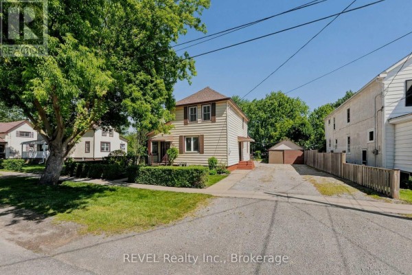 Exterior of the house with surrounding trees, green lawn, driveway, and a wooden fence. - 92 Saint Arnaud Street, Port Colborne