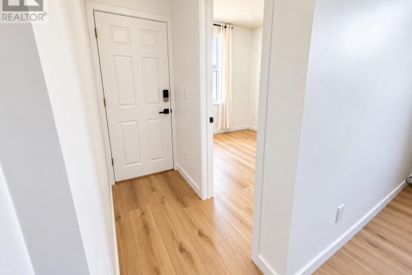 Hallway with light wood laminate flooring and white walls, showing a white interior door and a view into a room. - 920 Gladstone Avenue, Ottawa