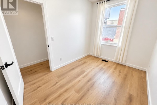 Empty room with white walls, light wood laminate flooring, and a window with white curtains. - 920 Gladstone Avenue, Ottawa