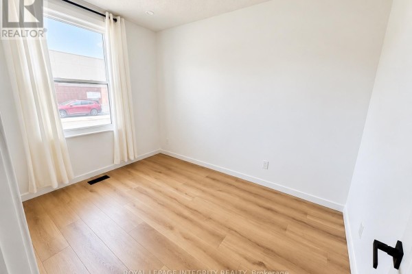 Empty room with white walls, light wood laminate flooring, and a window with white curtains on the left. - 920 Gladstone Avenue, Ottawa