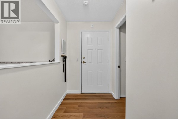 Apartment hallway with a white front door and wooden plank flooring. - 920 Glenwood Avenue Unit# 208, Kelowna